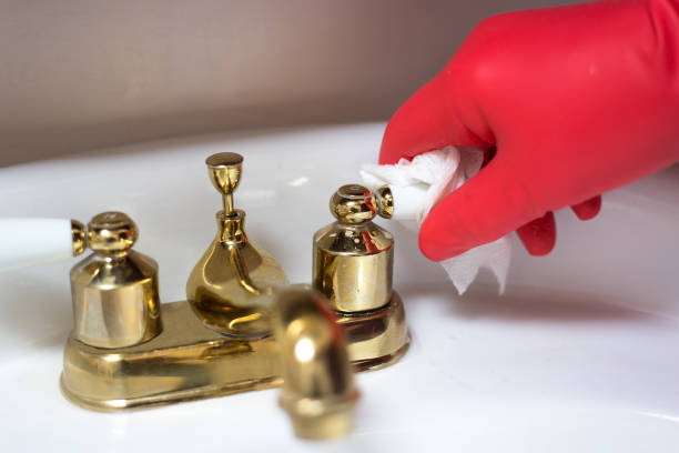 A gloved hand cleans a brass faucet with a cloth to restore its shine using household products.